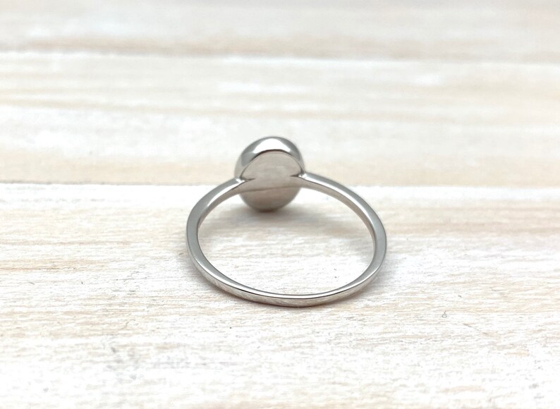 May include: A silver ring featuring a smooth, oval-shaped gemstone. The ring is simple and elegant.