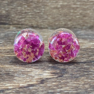 May include: A pair of round, clear resin ear gauges with pink and gold glitter embedded inside.