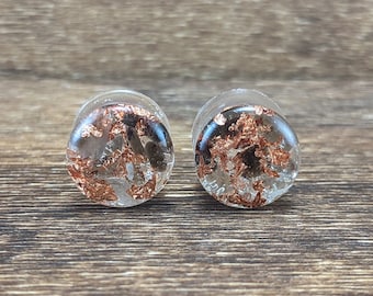 May include: A pair of clear round earrings with copper flakes embedded inside. The earrings are on a wooden surface.