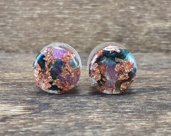 May include: A pair of clear, round earrings with embedded copper flakes and colorful accents. The earrings have a transparent appearance, showcasing the intricate details of the embedded materials. The earrings are displayed on a wooden surface.