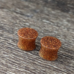 May include: Two brown and gold glitter ear gauges. The gauges are round and have a smooth, shiny finish.