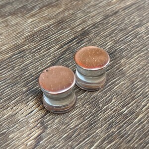 May include: Two pairs of brown and white acrylic ear gauges. The gauges are round and have a smooth finish.