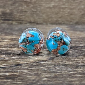 May include: A pair of round, clear resin earrings with turquoise and copper flakes embedded inside.