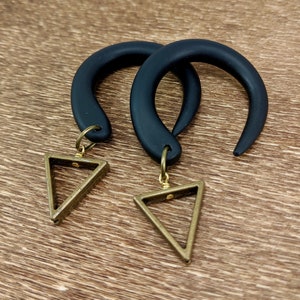 May include: A pair of black silicone ear gauges with gold triangle charms.