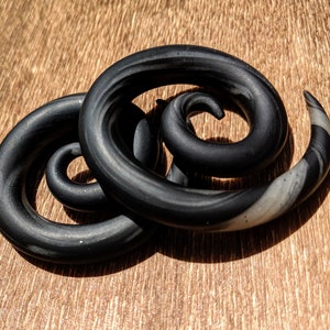 May include: A pair of black and white spiral ear gauges. The gauges are made of a smooth, shiny material and have a swirling pattern.