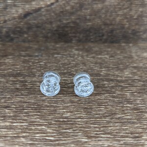 May include: Two clear glass ear gauges with a sparkly, glittery effect.
