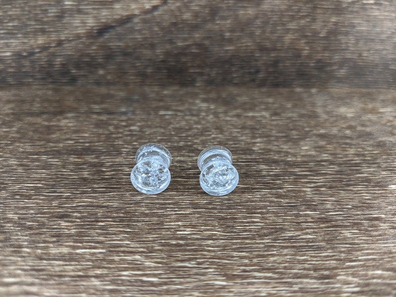 May include: Two clear glass ear gauges with a sparkly, glittery effect.