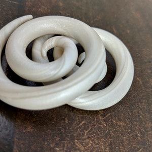 May include: Two white spiral ear gauges, made of wood, with a shiny finish.