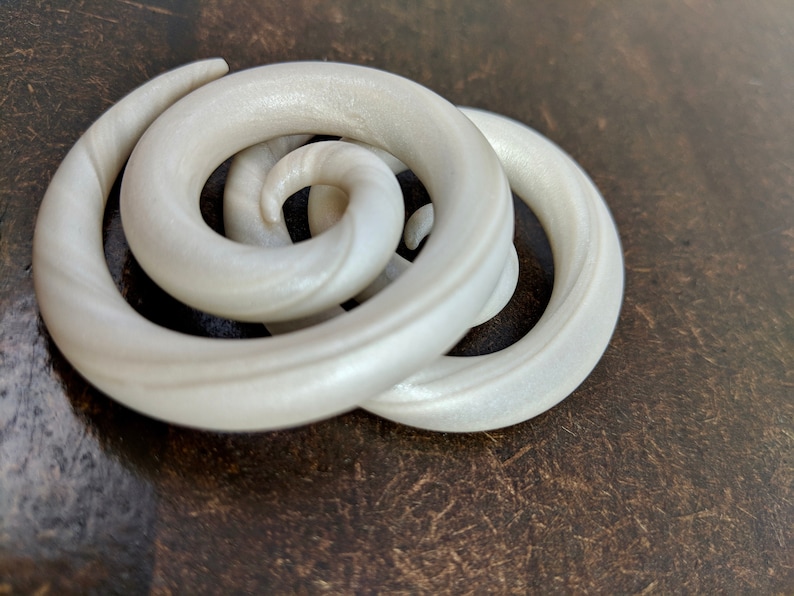 May include: Two white spiral ear gauges, made of wood, with a shiny finish.
