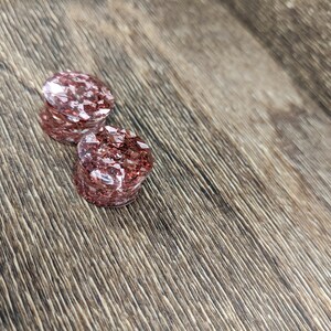 May include: Two round, clear, pink glitter ear gauges. The gauges are on a brown wooden surface.