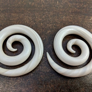 May include: A pair of white spiral ear gauges with a subtle shimmer. The gauges are made of a smooth, polished material and have a classic spiral design.