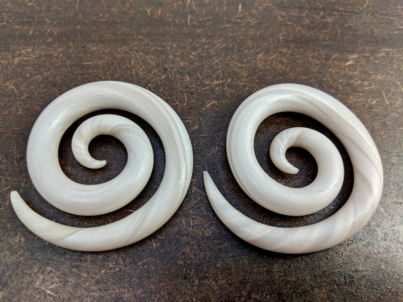 May include: A pair of white spiral ear gauges with a subtle shimmer. The gauges are made of a smooth, polished material and have a classic spiral design.