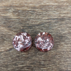 May include: Two round, red and silver glitter ear gauges. The gauges are made of resin and have a speckled appearance.