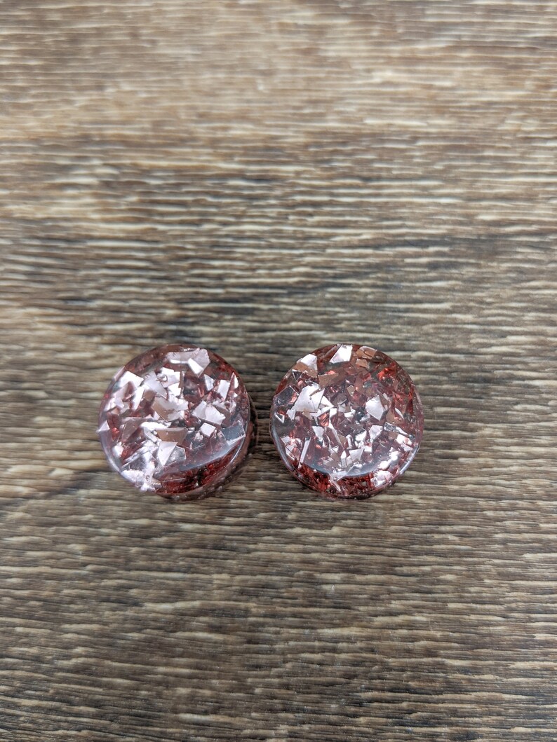 May include: Two round, red and silver glitter ear gauges. The gauges are made of resin and have a speckled appearance.