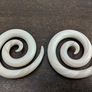 May include: A pair of white spiral ear gauges. The gauges are made of a smooth, white material with a subtle swirl pattern.