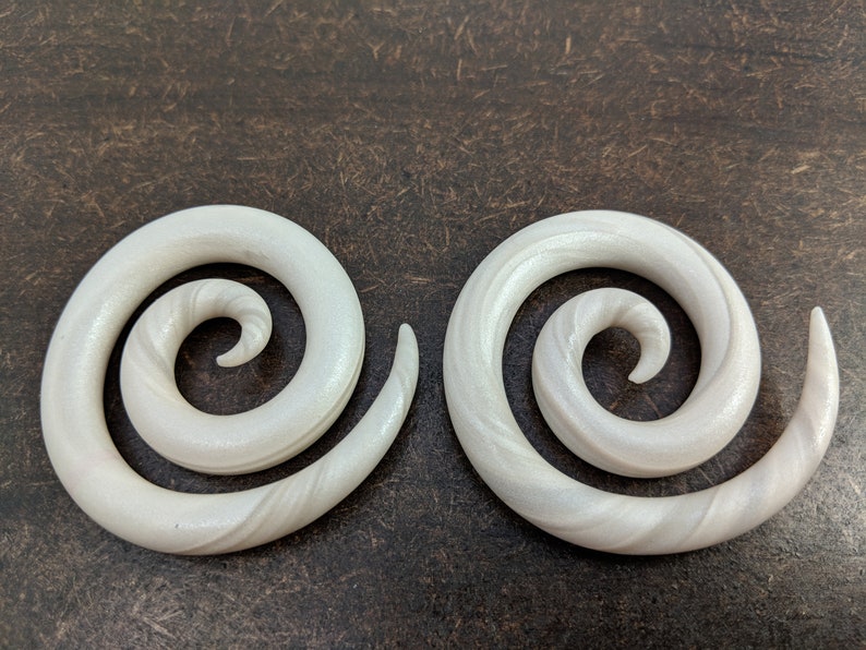 May include: A pair of white spiral ear gauges. The gauges are made of a smooth, white material with a subtle swirl pattern.