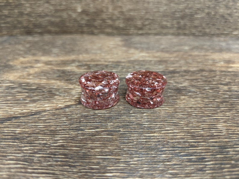May include: Two round, red and gold glitter ear gauges. The gauges are made of resin and have a speckled appearance.