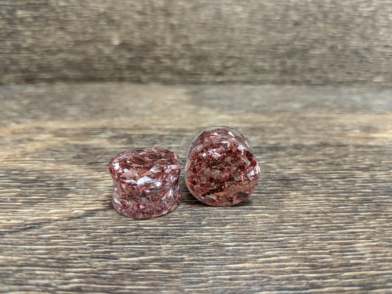 May include: Two round, clear, resin ear gauges with a copper-colored, metallic flake design.