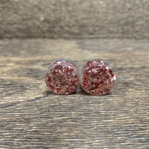 May include: A pair of clear glass ear gauges with a red and gold glitter design.