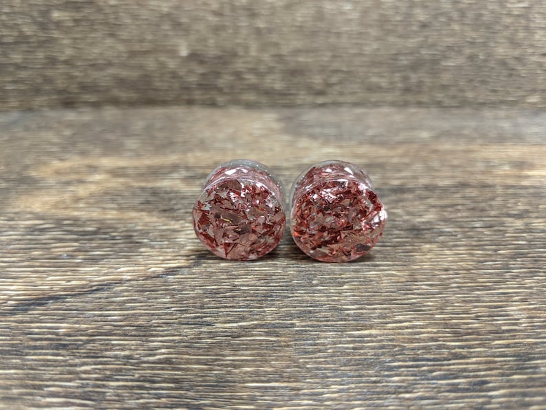 May include: A pair of clear glass ear gauges with a red and gold glitter design.
