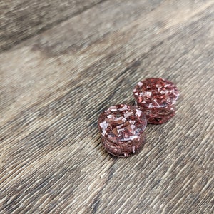 May include: A pair of red and gold glitter ear gauges. The gauges are made of clear resin with embedded glitter.