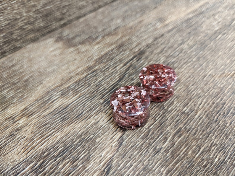 May include: A pair of red and gold glitter ear gauges. The gauges are made of clear resin with embedded glitter.