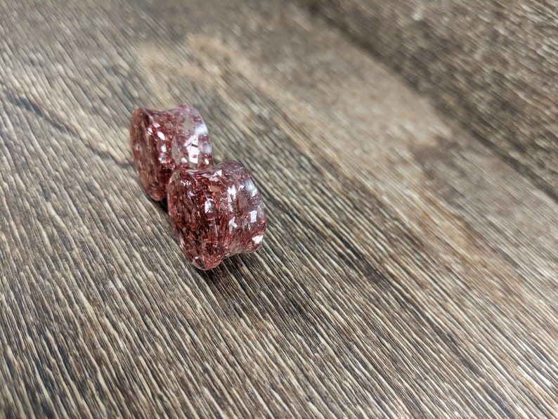 May include: Two clear resin ear gauges with a red and gold glitter embedded inside.
