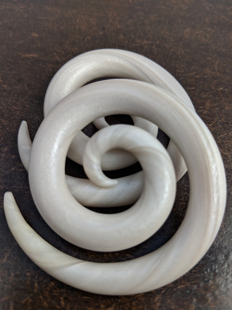 May include: A pair of white spiral ear gauges made of acrylic. The gauges have a pearlescent finish and are designed to stretch the earlobe.