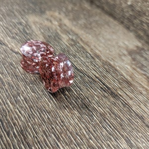 May include: Two pink and clear glass ear gauges with a glittery finish. The gauges are on a wood surface.