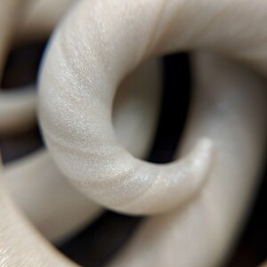 May include: Close-up of a white, textured, 3D printed object. The object is shaped like a series of interlocking loops.