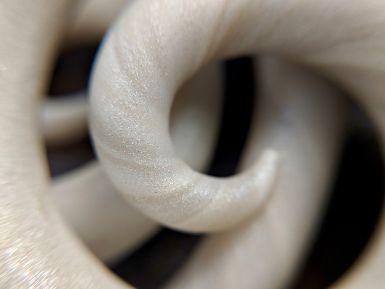 May include: Close-up of a white, textured, 3D printed object. The object is shaped like a series of interlocking loops.