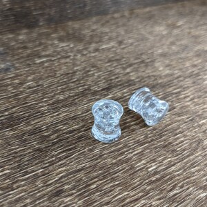 May include: Two clear glass ear gauges with a textured surface.