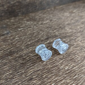 May include: Two clear glass ear gauges with a sparkly, speckled finish.