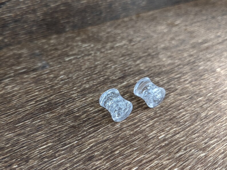 May include: Two clear glass ear gauges with a sparkly, speckled finish.