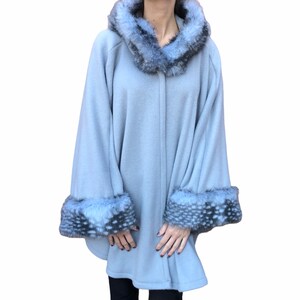 May include: A light gray hooded cape with a faux fur trim around the hood and cuffs. The cape has a button closure in the front.