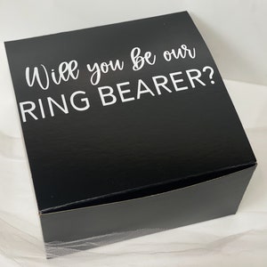 May include: Black gift box with white text that reads "Will you be our RING BEARER?"