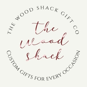 May include: The Wood Shack Gift Co. logo with the text "The Wood Shack" in a rose gold font. The text is in a circle with the words "The Wood Shack Gift Co. Custom Gifts for Every Occasion" around the outside.