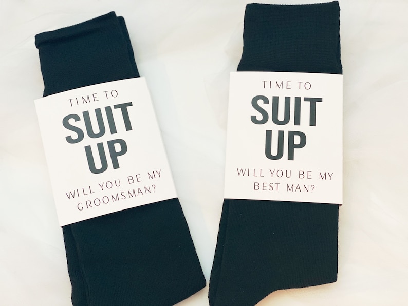 May include: Two pairs of black socks with white cards attached to them. The cards say "Time to Suit Up" and ask "Will you be my groomsman?" and "Will you be my best man?"