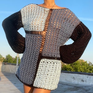May include: A black and grey crochet sweater with a loose fit and long sleeves. The sweater has a unique patchwork design with different sized squares.