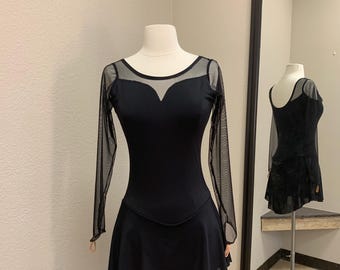 Op de afbeelding: Zwarte kunstschaatsjurk met een mesh halslijn en mouwen. De jurk heeft een sweetheart halslijn en een uitlopende rok. De jurk wordt op een mannequin gepresenteerd.