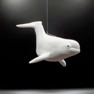 May include: A white ceramic whale sculpture hanging from a string. The whale is facing the right side of the image and has a slightly open mouth.