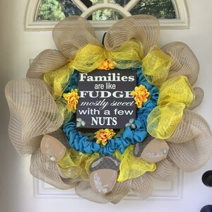 May include: A decorative wreath with a sign that reads "Families are like fudge mostly sweet with a few nuts." The wreath features tan mesh, yellow accents, and a teal base. Decorative acorns and flowers are also included.