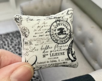 May include: A small white pillow with a black and white vintage postage stamp design. The pillow has the text "Les belles lettres de la province" and "M. LEJEUNE" printed on it.