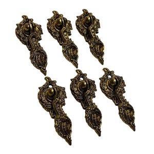May include: Six antique-style bronze drawer pulls. Each pull features an ornate design with a rounded top, a central sphere, and a detailed, elongated lower section. The pulls are arranged on a white background.