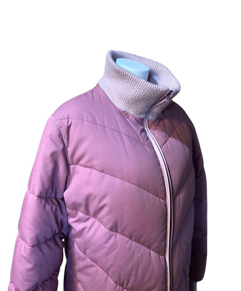 May include: A mauve puffer jacket with a high, ribbed collar and a full-length zipper. The jacket has a quilted design with diagonal stitching and a light pink trim. The collar is a light gray color.