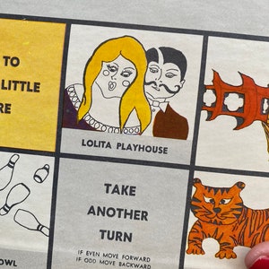 May include: A vintage game board with a colorful illustration of a couple in a playhouse, a tiger in a circus, and bowling pins. The text on the board reads "Lolita Playhouse", "Take Another Turn", "If even move forward, if odd move backward", and "Circus".