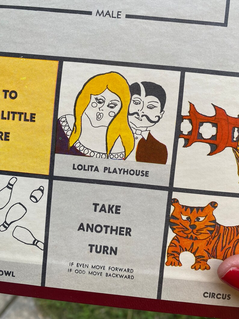 May include: A vintage game board with a colorful illustration of a couple in a playhouse, a tiger in a circus, and bowling pins. The text on the board reads "Lolita Playhouse", "Take Another Turn", "If even move forward, if odd move backward", and "Circus".