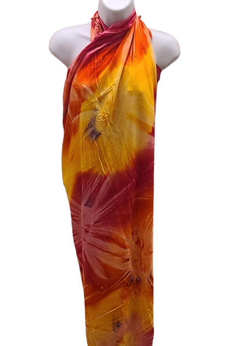 May include: A yellow, orange, and pink sarong with a tie-dye pattern. The sarong is draped over a mannequin.