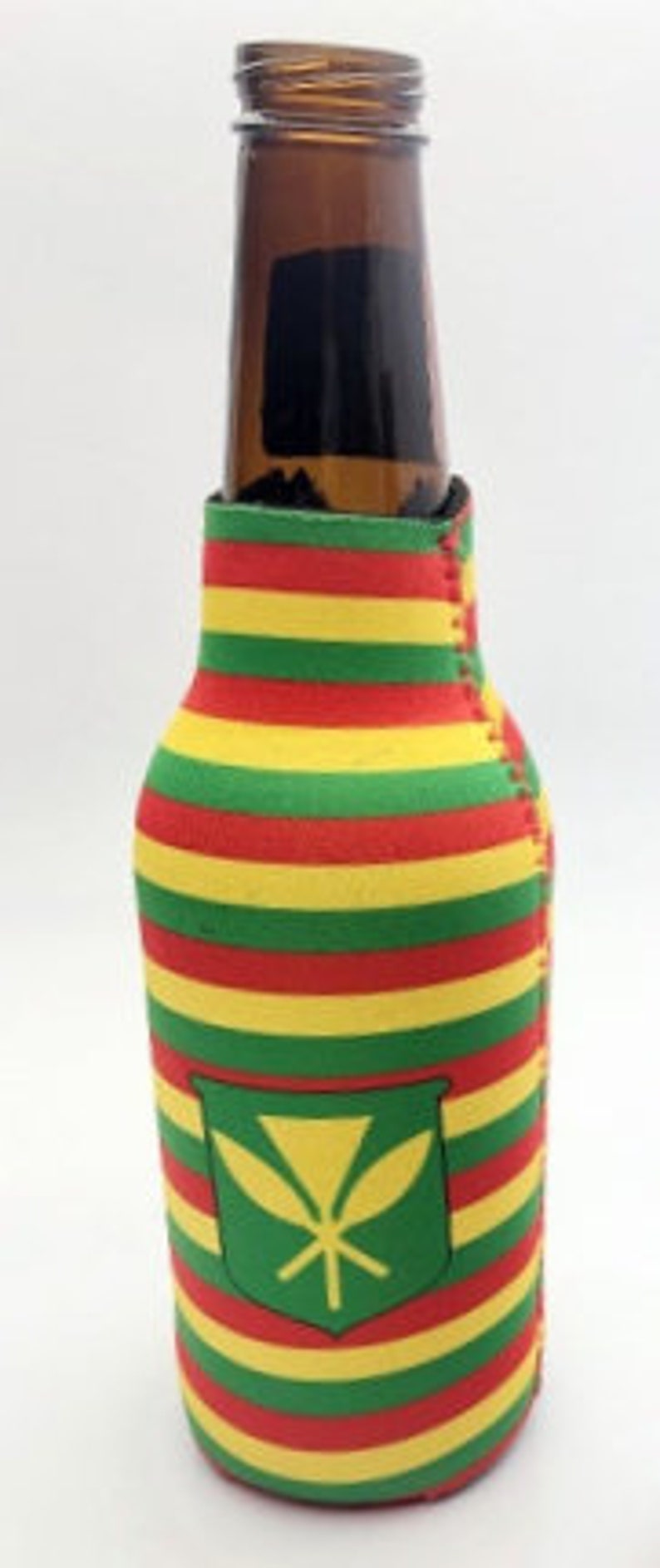 May include: A brown glass bottle inside a colorful beer can cooler. The cooler has horizontal stripes in red, yellow, and green. A green patch with a yellow leaf design is on the front of the cooler. The bottle is empty.