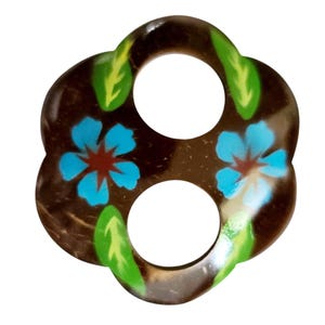 May include: A brown, flower-shaped button with two holes. The button features blue flower designs with red centers and green leaves. The button is made of a natural material and has a glossy finish.